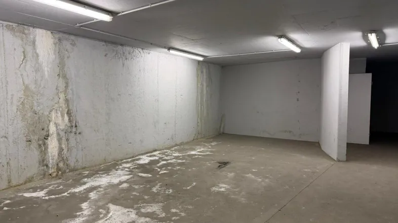Geräumiger Kellerraum mit Betonwänden und -boden, ausgestattet mit einfacher Beleuchtung und sichtbaren Gebrauchsspuren.