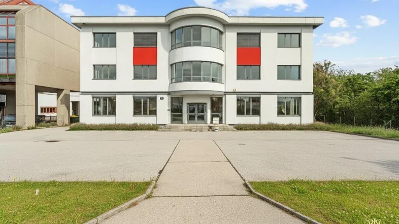 Modernes Bürogebäude mit weißer Fassade, roten Akzenten und großem Parkplatz davor.
