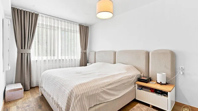 Helles Schlafzimmer mit großem Bett, Holzboden und Vorhängen für angenehme Lichtverhältnisse.