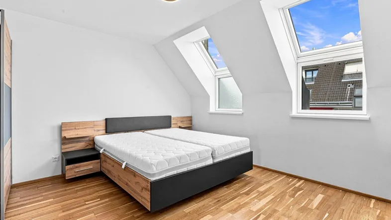 Helles Schlafzimmer mit Holzboden, Dachschrägen und zwei Dachfenstern, die viel Licht hereinlassen.