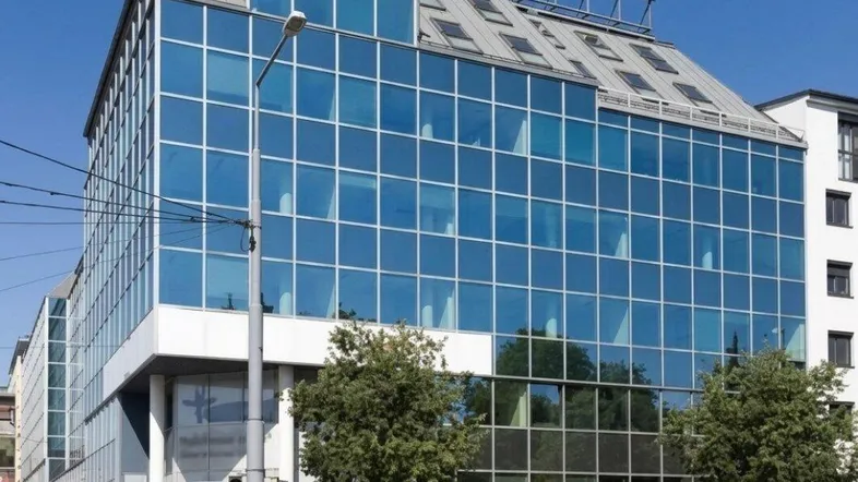 Modernes Bürogebäude mit blauer Glasfassade und großen Fenstern an einer städtischen Straße.
