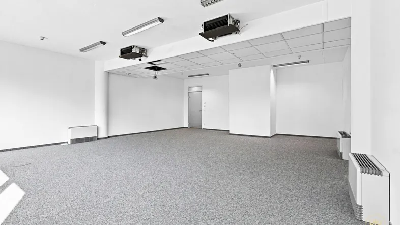 Geräumiger, leerer Büroraum mit grauem Teppichboden, weißen Wänden und abgehängter Decke.