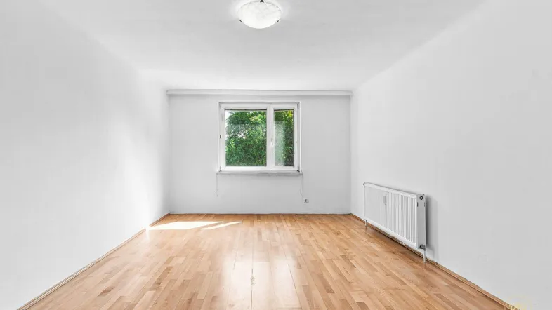 Helles, leeres Zimmer mit Parkettboden und einem Fenster mit Blick ins Grüne.