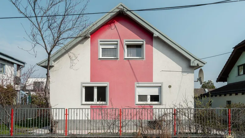 Vorderansicht eines Einfamilienhauses mit roter Fassadenakzentuierung, Satteldach und Rollläden an den Fenstern.
