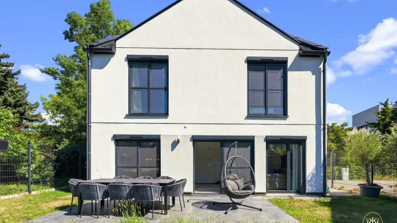 Moderne Hausrückseite mit großer gepflasterter Terrasse, Gartenmöbeln und Schaukelstuhl.