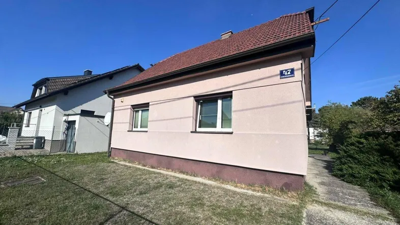 Einfaches Einfamilienhaus mit rosafarbener Fassade und Satteldach in ländlicher Umgebung.