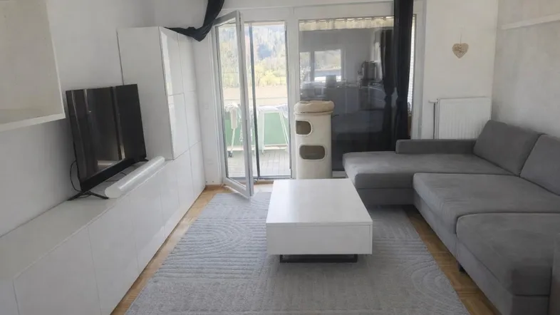 Helles Wohnzimmer mit modernem Sofa, weißem TV-Möbel und Zugang zum Balkon mit Bergblick.