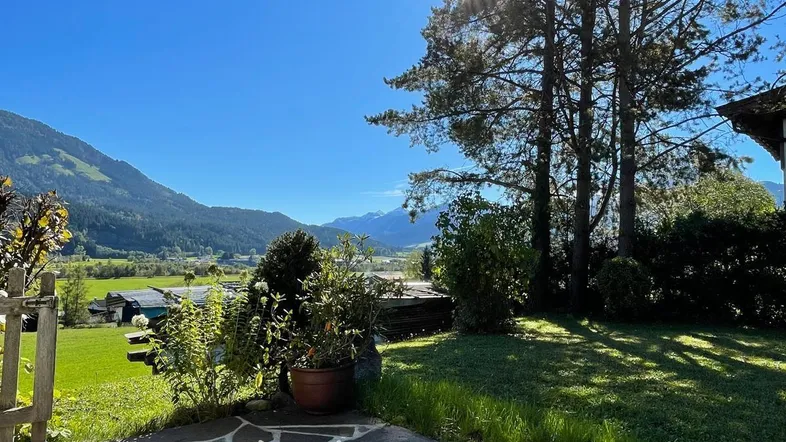 Sonnige Steinterrasse mit Rasenfläche und weitem Blick auf die umliegende Berglandschaft.