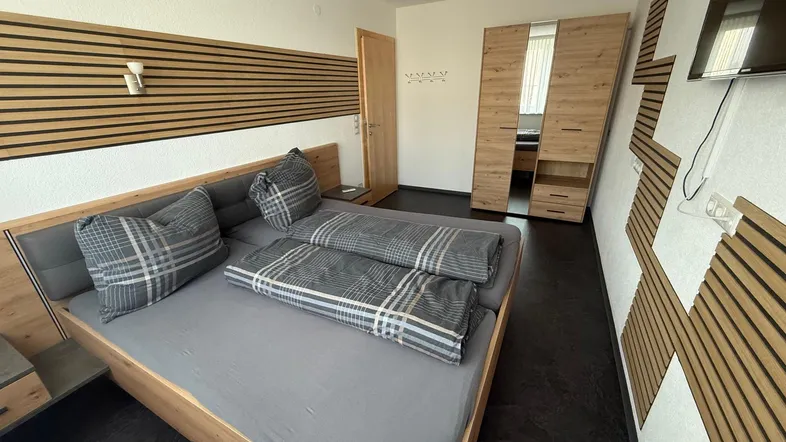 Modernes Schlafzimmer mit Holzbett, dunklem Boden und dekorativen Wandpaneelen.