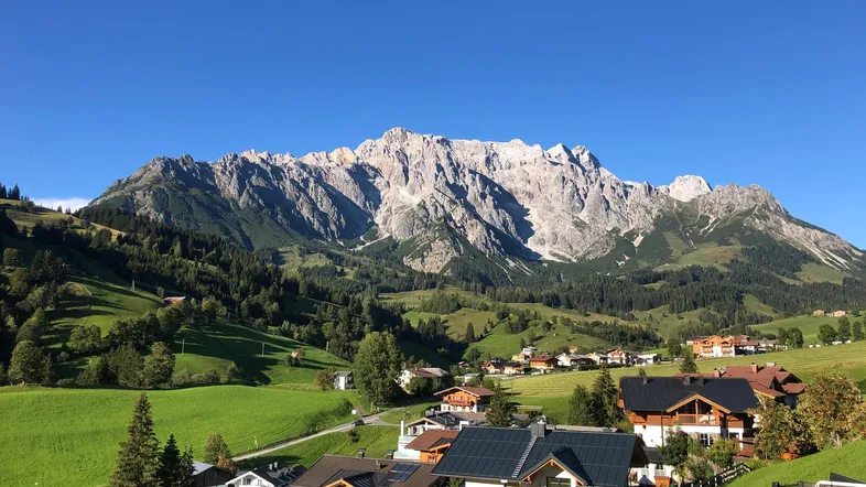 Panoramablick auf die majestätischen Berge und ein idyllisches Dorf in grüner Landschaft.