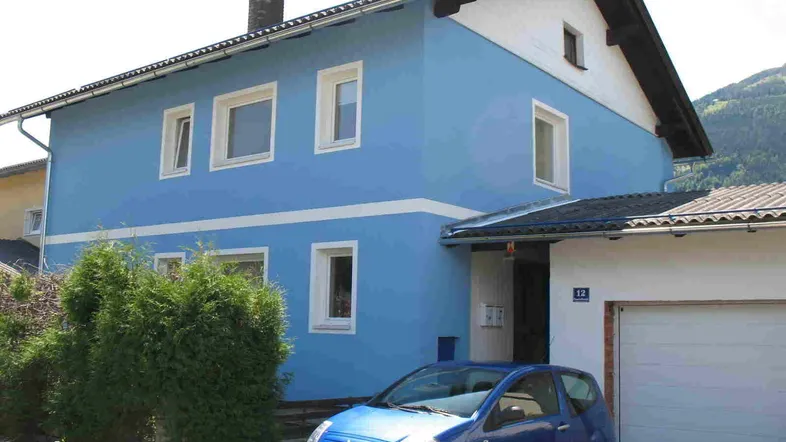 Blau gestrichenes Einfamilienhaus mit weißem Akzent und integrierter Garage an einem sonnigen Tag.