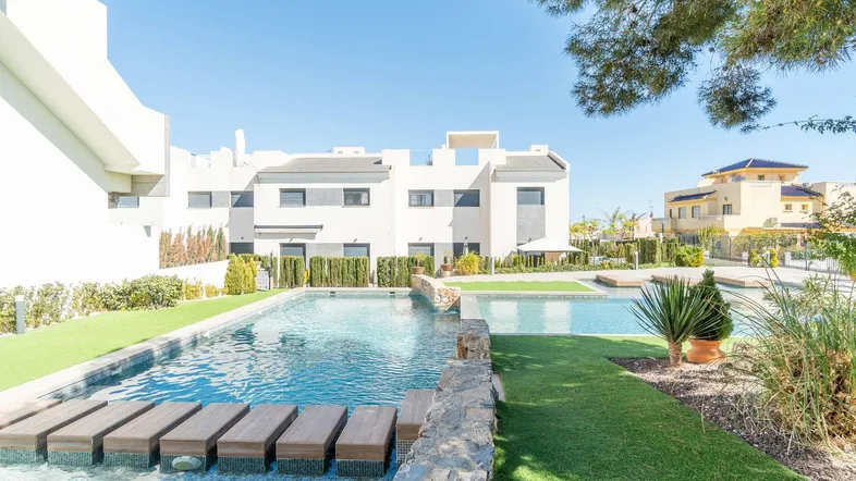 Moderne Wohnanlage mit großem Gemeinschaftspool, umgeben von Kunstrasen und mediterraner Bepflanzung.