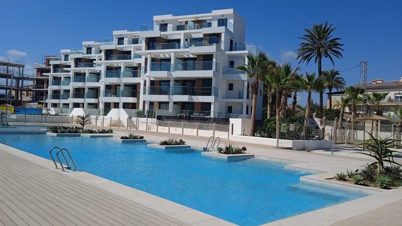 Modernes Apartmentgebäude mit großem Poolbereich und Palmen unter strahlend blauem Himmel.