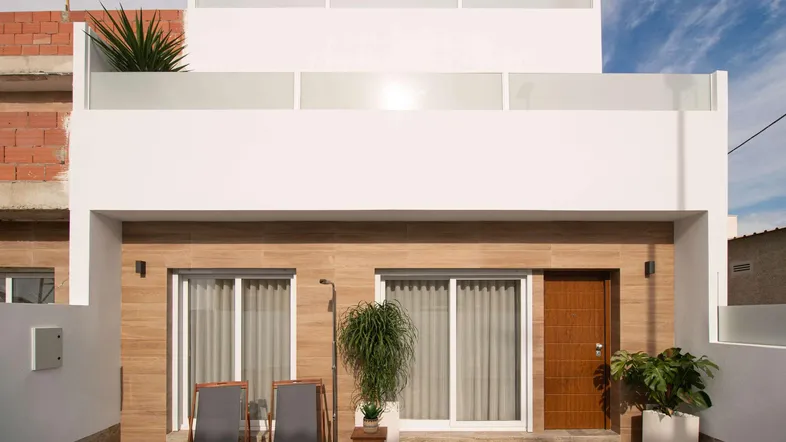 Moderne Hausfassade mit hellem Anstrich, Holzverkleidung und einer kleinen Terrasse mit Liegestühlen.