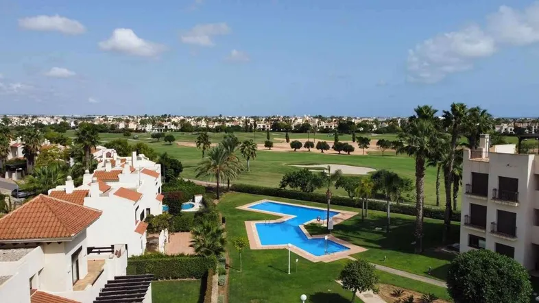 Panoramablick auf die Wohnanlage mit großem Poolbereich und angrenzendem Golfplatz.
