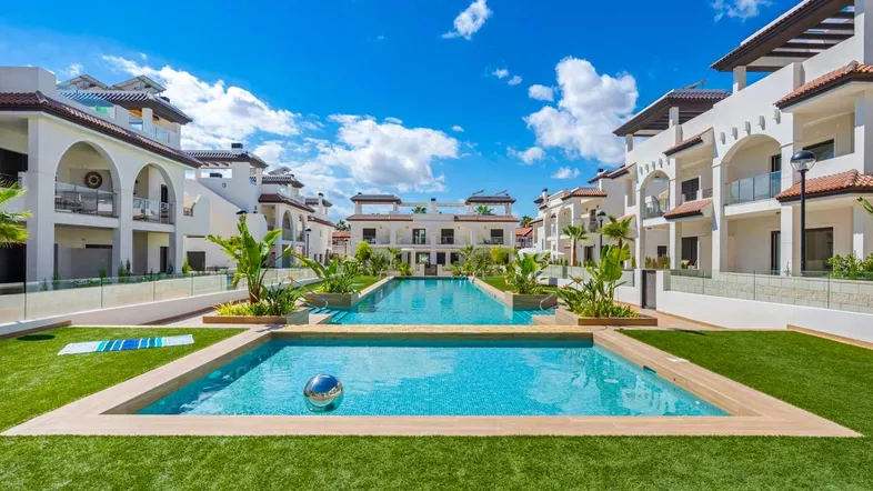 Weitläufige Poolanlage mit mehreren Schwimmbecken und gepflegten Grünflächen zwischen modernen Wohngebäuden.