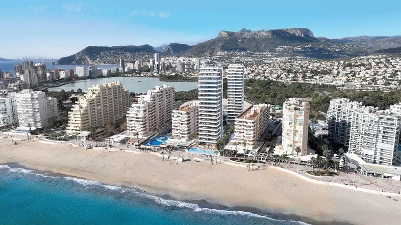 Luftaufnahme einer Küstenstadt mit modernen Hochhäusern, Sandstrand und Bergen im Hintergrund bei Tageslicht.