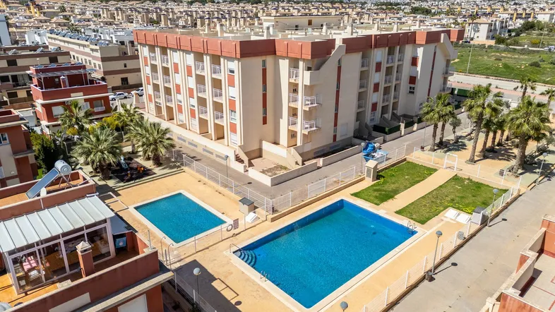 Luftaufnahme eines Wohnkomplexes mit mehreren Gebäuden, zwei Pools und umliegender Wohnbebauung.