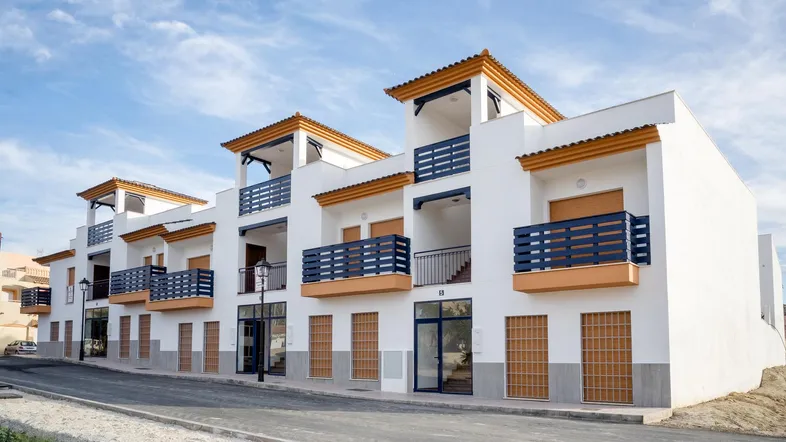 Moderne Wohnanlage mit weißer Fassade, blauen Balkongeländern und orangefarbenen Akzenten unter blauem Himmel.