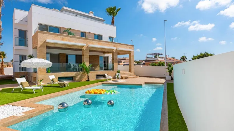 Moderne Villa mit großem Pool, Sonnenterrasse und gepflegtem Rasen unter blauem Himmel.