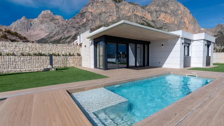 Moderne Villa mit privatem Pool, Holzterrasse und beeindruckendem Bergblick unter blauem Himmel.