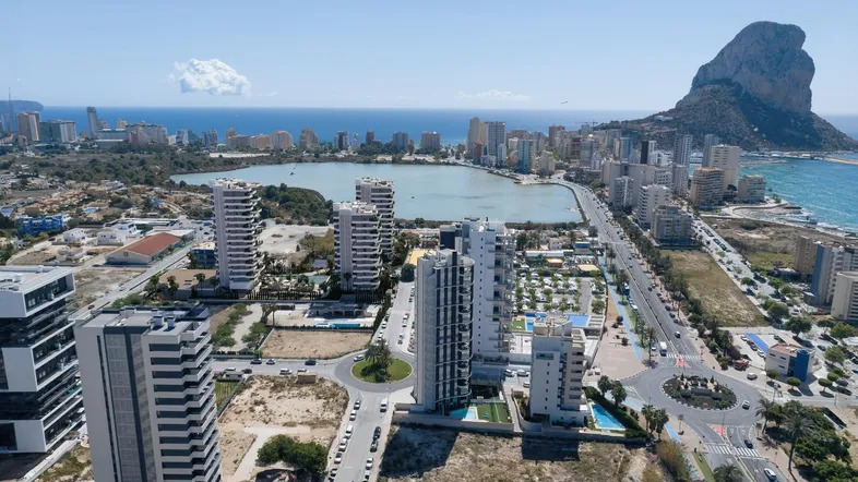 Luftaufnahme einer Küstenstadt mit modernen Hochhäusern, einem See und dem Meer im Hintergrund.
