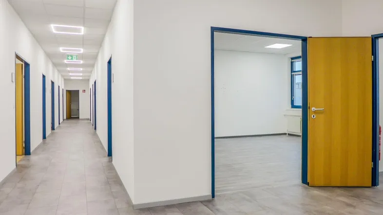 Langer, heller Flur mit mehreren Türen und modernen Deckenleuchten, der zu Büroräumen führt.