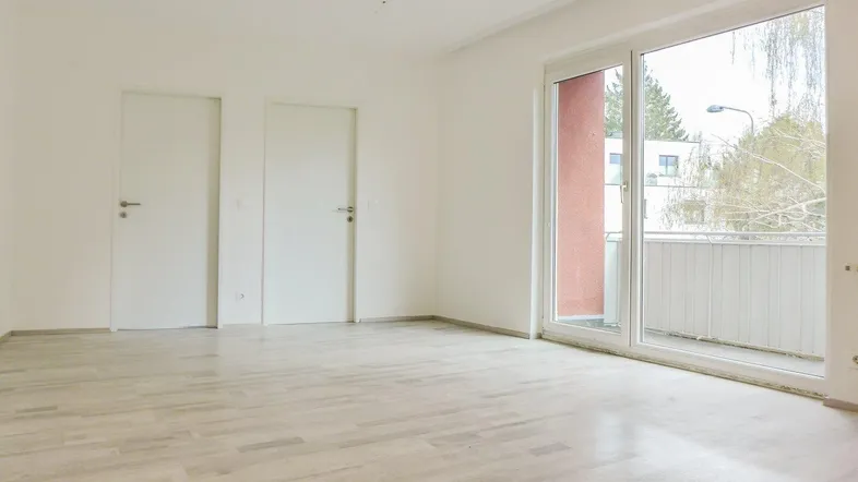 Helles, leeres Zimmer mit Parkettboden und Zugang zu einem Balkon, ideal als Wohnbereich.
