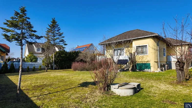 Großer Gartenbereich mit Rasenfläche, Bäumen und einem Brunnen vor dem Haus.