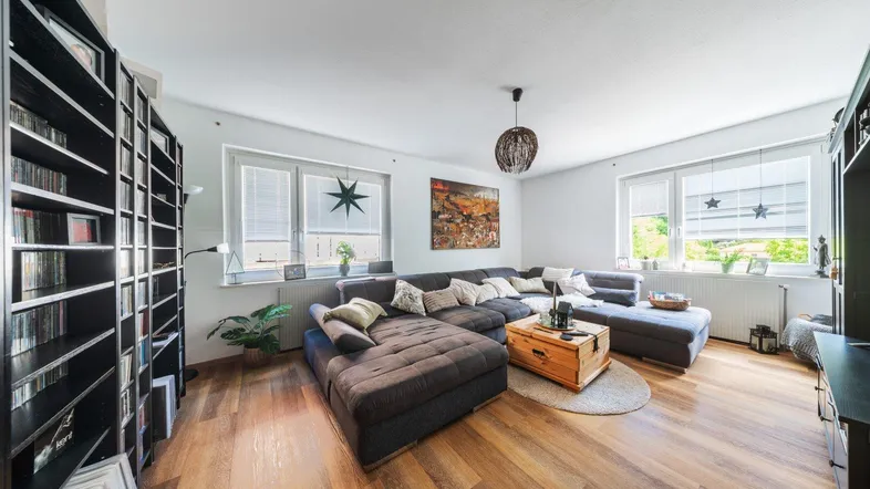Geräumiges Wohnzimmer mit großem Ecksofa, Holzboden und zwei Fenstern.