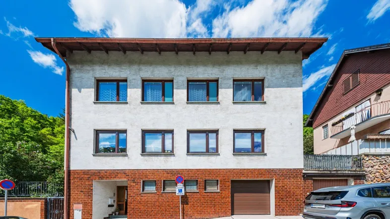 Mehrfamilienhaus mit weißer Fassade, roten Ziegeln und integrierter Garage unter blauem Himmel.