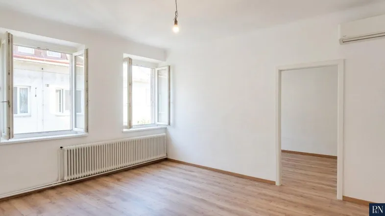 Helles, unmöbliertes Zimmer mit Laminatboden, zwei Fenstern und Heizkörper.