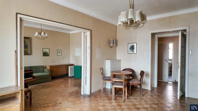 Geräumiges Wohnzimmer mit Parkettboden, Kronleuchter und Zugang zu einem weiteren Raum.