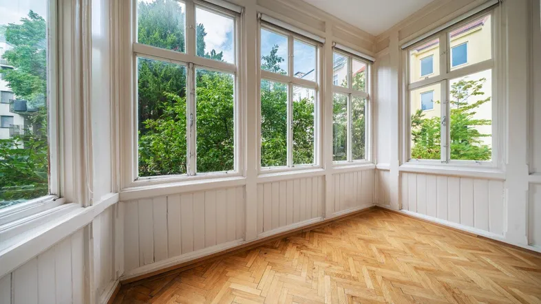 Heller Wintergarten mit großen Fenstern, Fischgrätparkett und einem schönen Blick ins Grüne.