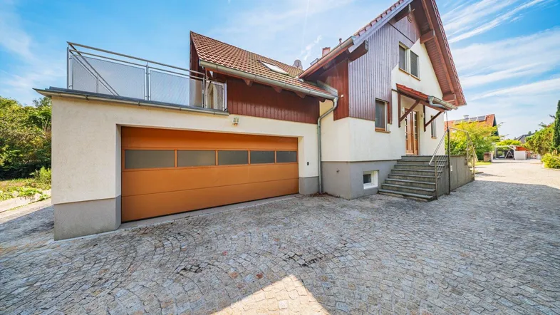 Einfamilienhaus mit integrierter Garage, gepflasterter Auffahrt und Balkon im Obergeschoss.