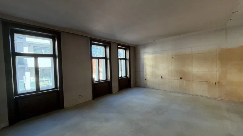 Geräumiger, unmöblierter Raum mit drei Fenstern und Rohbauwänden, bereit für den Ausbau.