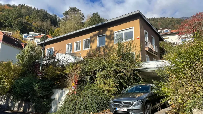 Hausfassade mit üppiger Bepflanzung und einem Carport, eingebettet in eine grüne Umgebung.