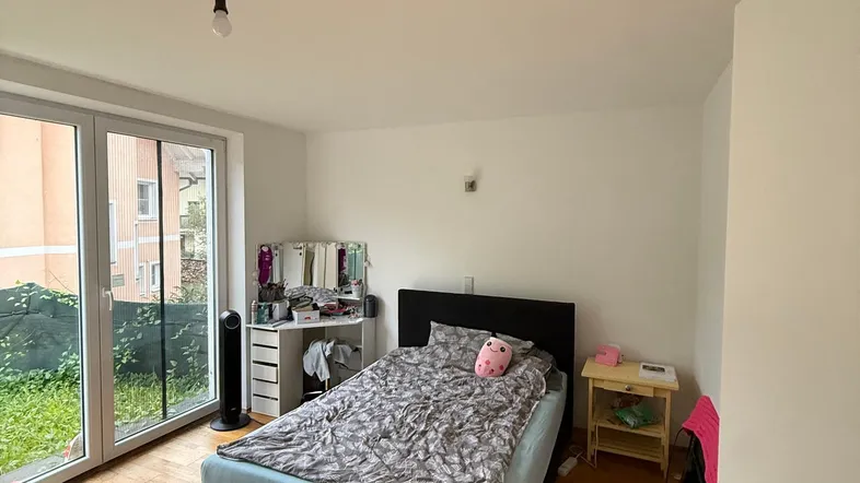 Helles Schlafzimmer mit Holzboden, großem Fenster und direktem Zugang zum Gartenbereich.