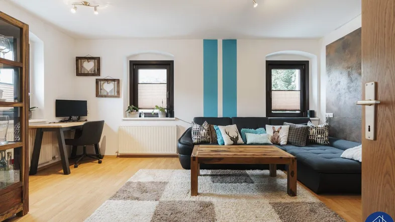 Helles Wohnzimmer mit Holzboden, gemütlichem Sofa und integriertem Arbeitsbereich am Fenster.