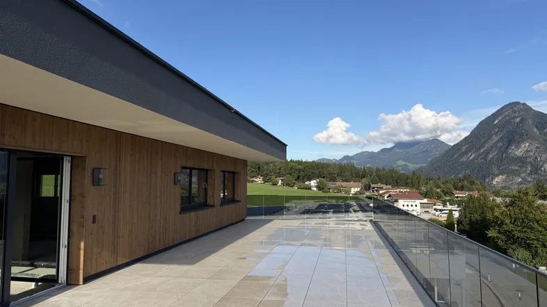Geräumige Dachterrasse mit Fliesenboden und Glasgeländer, bietet einen weiten Blick auf die umliegenden Berge.