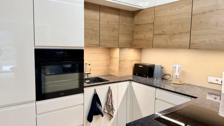 Moderne Küche mit weißen Hochglanzfronten, Holzdetails und dunkler Arbeitsplatte.