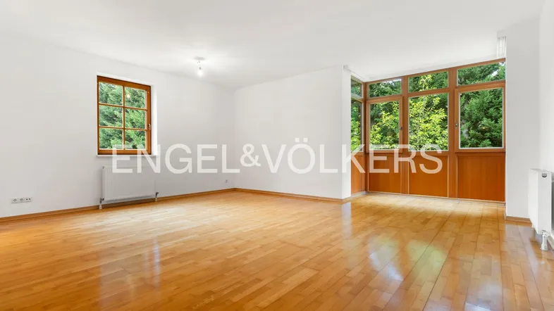 Helles Wohnzimmer mit Parkettboden, weißen Wänden und großen Fenstern mit Blick ins Grüne.