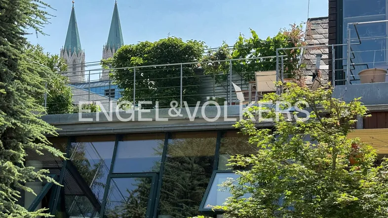 Dachterrasse mit Sitzgelegenheiten und Blick auf die Kirchtürme, umgeben von grünen Bäumen.