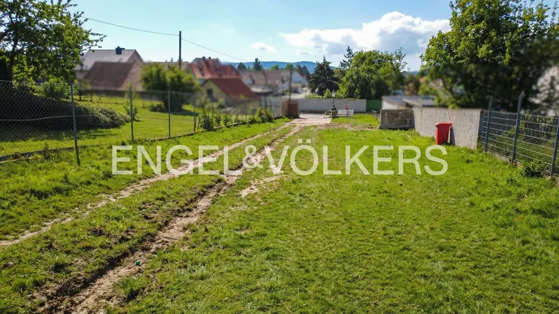 Grünfläche mit Zufahrtsweg und Blick auf umliegende Häuser in ländlicher Umgebung.