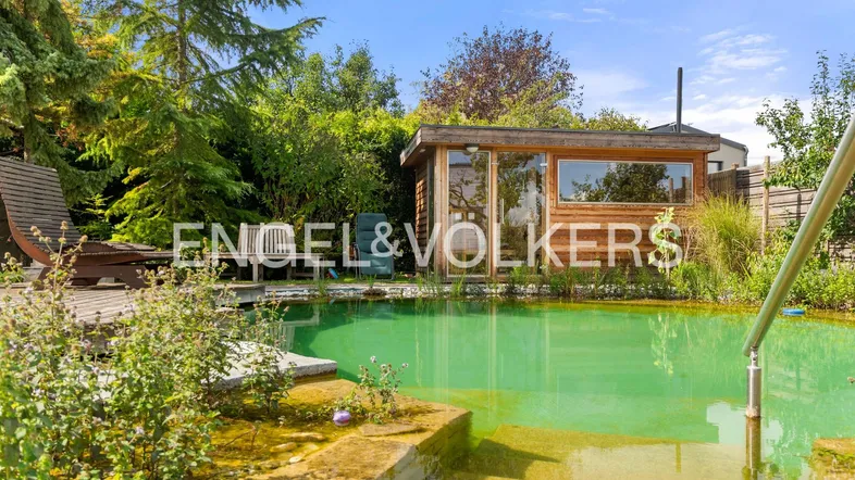 Natürlicher Schwimmteich mit Holzhaus und üppiger Bepflanzung im weitläufigen Gartenbereich.