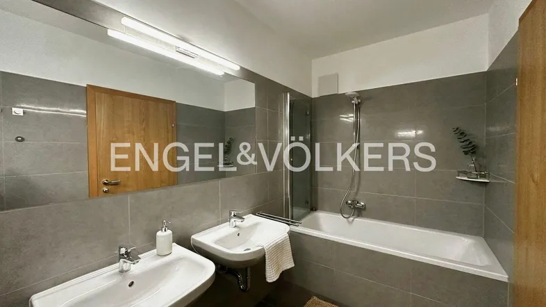 Modernes Badezimmer mit zwei Waschbecken, Badewanne und Duschfunktion, komplett gefliest in Grau.