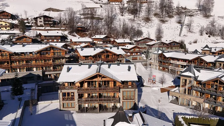 Winterliche Ansicht eines Bergdorfes mit verschneiten Dächern und Chalets in alpiner Landschaft.