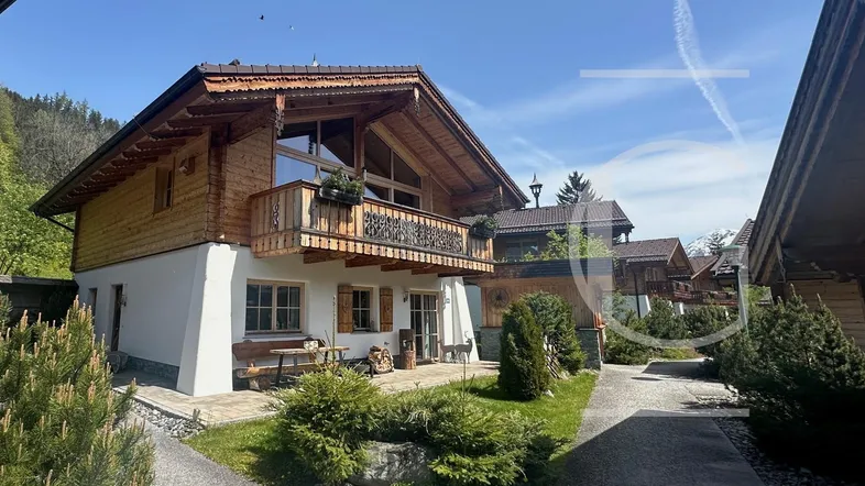 Charmantes Chalet-Haus mit Holzbalkonen, weißer Fassade und gepflegtem Gartenbereich.