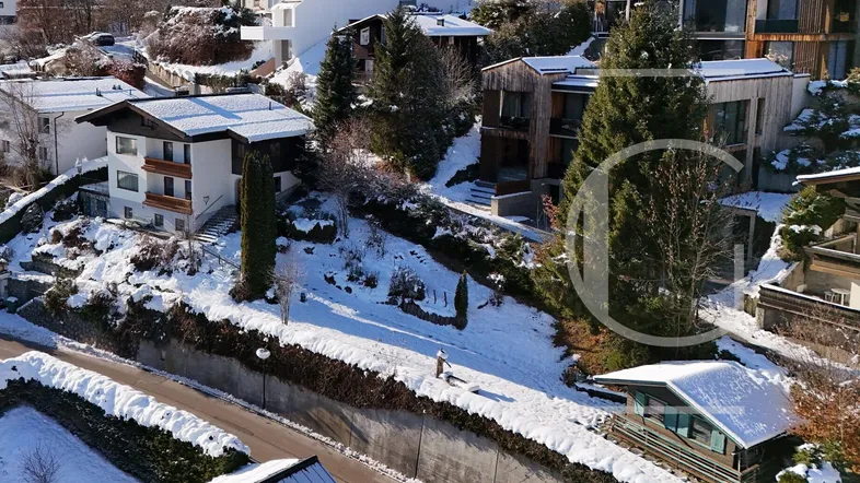 Luftaufnahme einer Wohnsiedlung in verschneiter Berglandschaft mit mehreren Häusern und Bäumen.