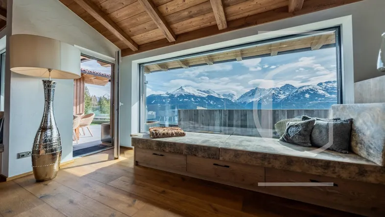 Gemütlicher Wohnbereich mit großer Fensterfront, Holzbalkendecke und atemberaubendem Bergblick.